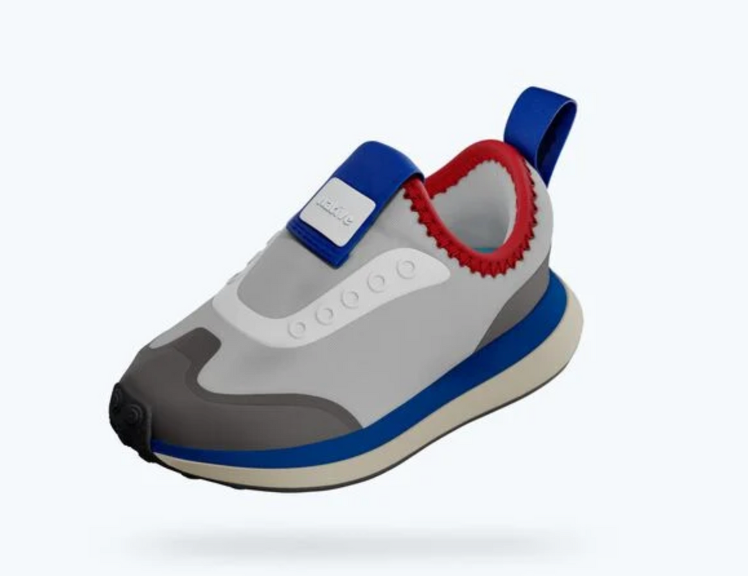 A children's slip-on sneaker in light gray, blue, and red, featuring a hook-and-loop strap closure, a pull tab, and a thick sole.