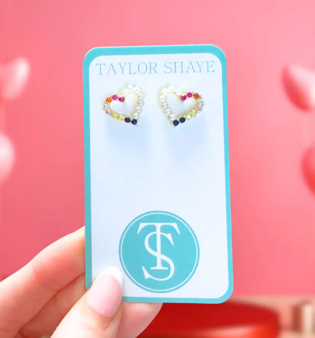 Heart-shaped earrings on a Taylor Shaye card against a pink background