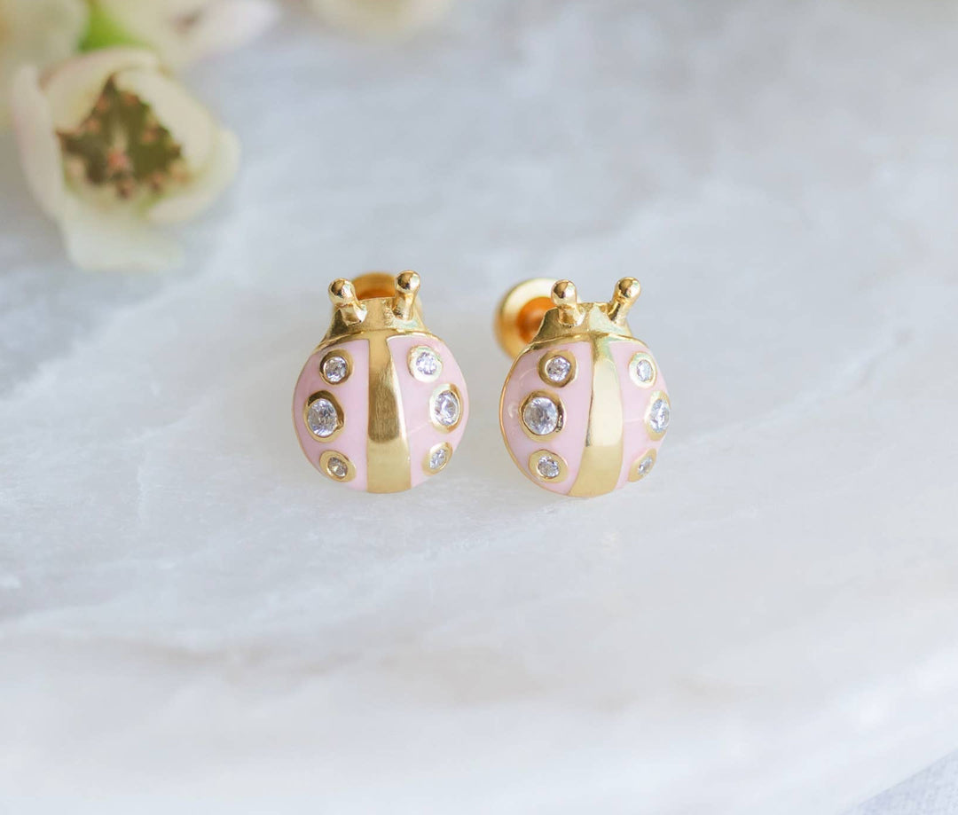 Gold and pink earrings on a marble surface with white flowers in the background