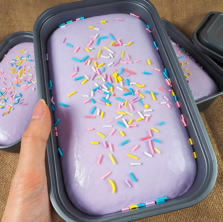 Purple ice cream with colorful sprinkles in a container on a brown surface