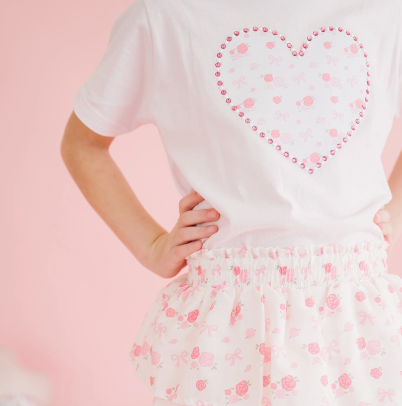 girl wearing a white t-shirt with a pink heart design and a floral skirt on a pink background