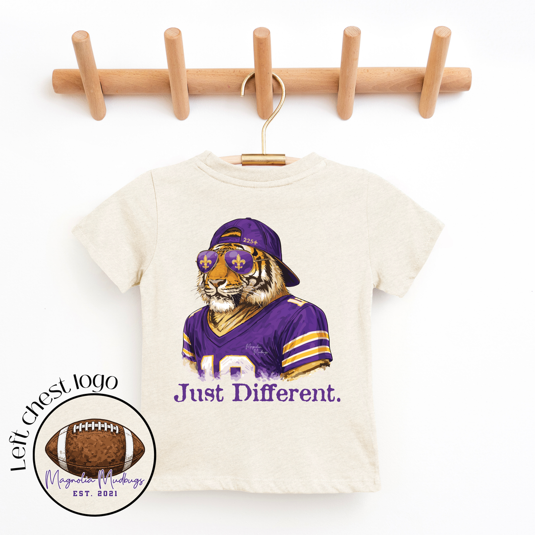 T-shirt with tiger wearing a purple sports jersey and sunglasses, text 'Just Different', on a wooden hanger.