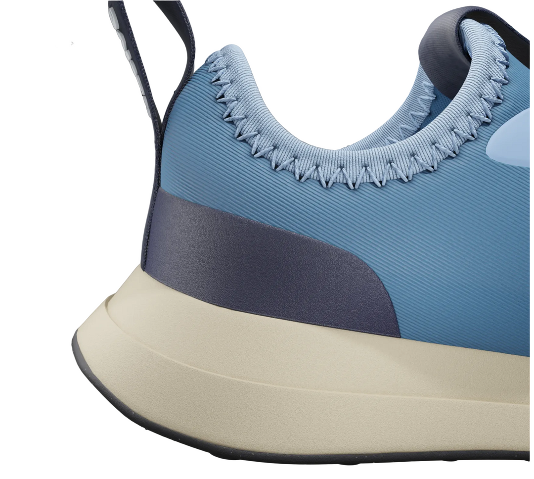A close-up of a sneaker in light blue, dark gray, and cream, shown against a blurred e-commerce product page background.