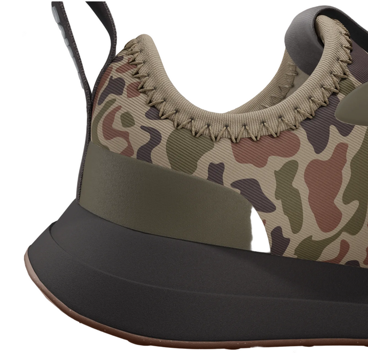 A close-up of a sneaker shown on a product page, featuring a beige, green, and brown camouflage pattern on the upper, a thick olive green midsole band, and a dark gray outsole.