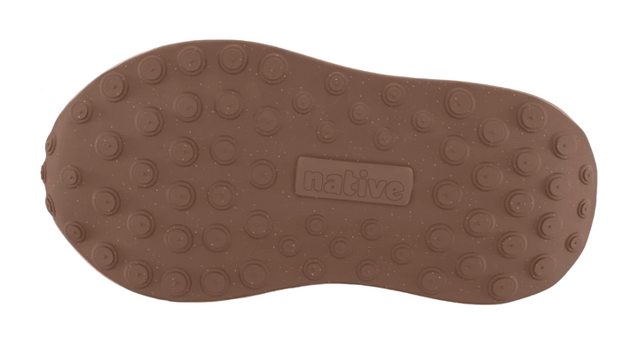 A close-up of a brown shoe sole with circular tread patterns and a central embossed 'native' logo, shown against a dim gray background.