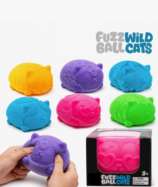 Colorful 'NEEDOH FUZZWILD BALL CATS' toys on a white background with a hand holding a purple toy.