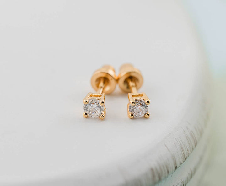 Gold stud earrings with clear gemstones on a light background