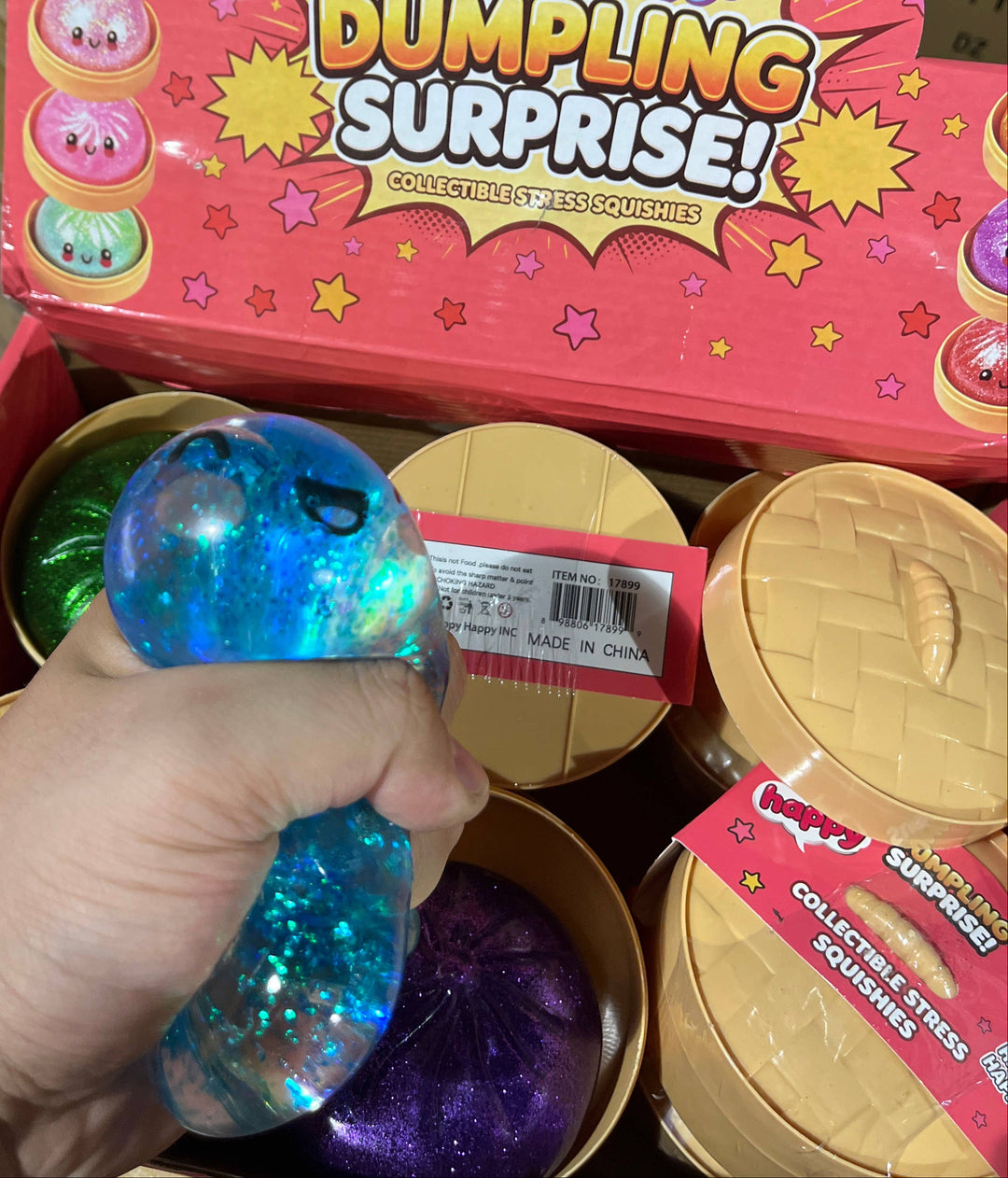 Happy Dumpling Surprise toy packaging with a hand holding a blue glittery toy.