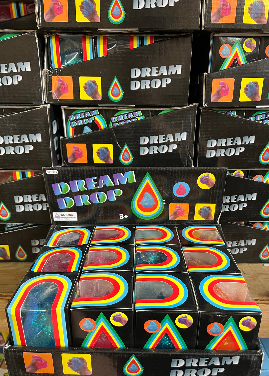 Display of 'Dream Drop' product packaging with colorful designs on a wooden surface.