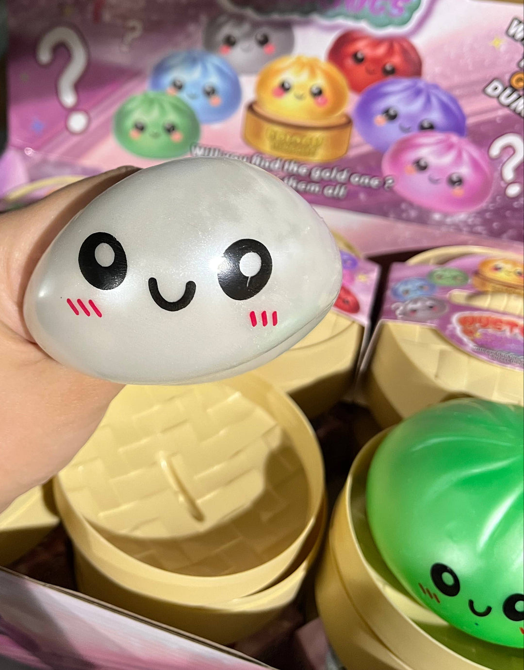 dumpling with a happy face design held by a hand, with colorful toy packaging in the background.