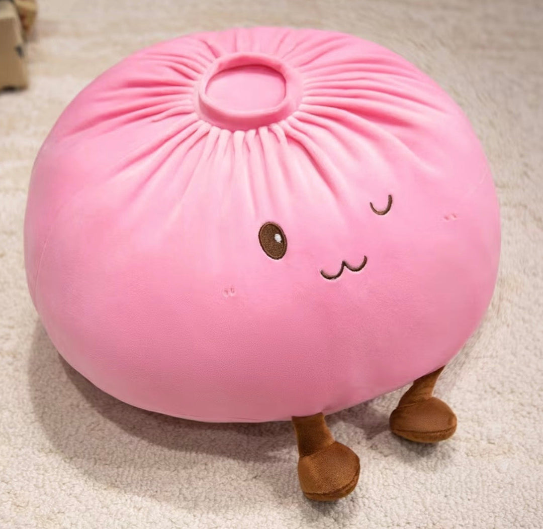 A pink plush dumpling pillow with embroidered facial features and small brown legs, resting on a light beige carpet.