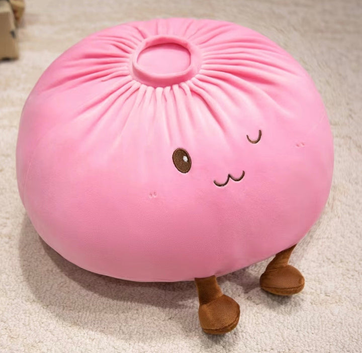 A pink plush dumpling pillow with embroidered facial features and small brown legs, resting on a light beige carpet.